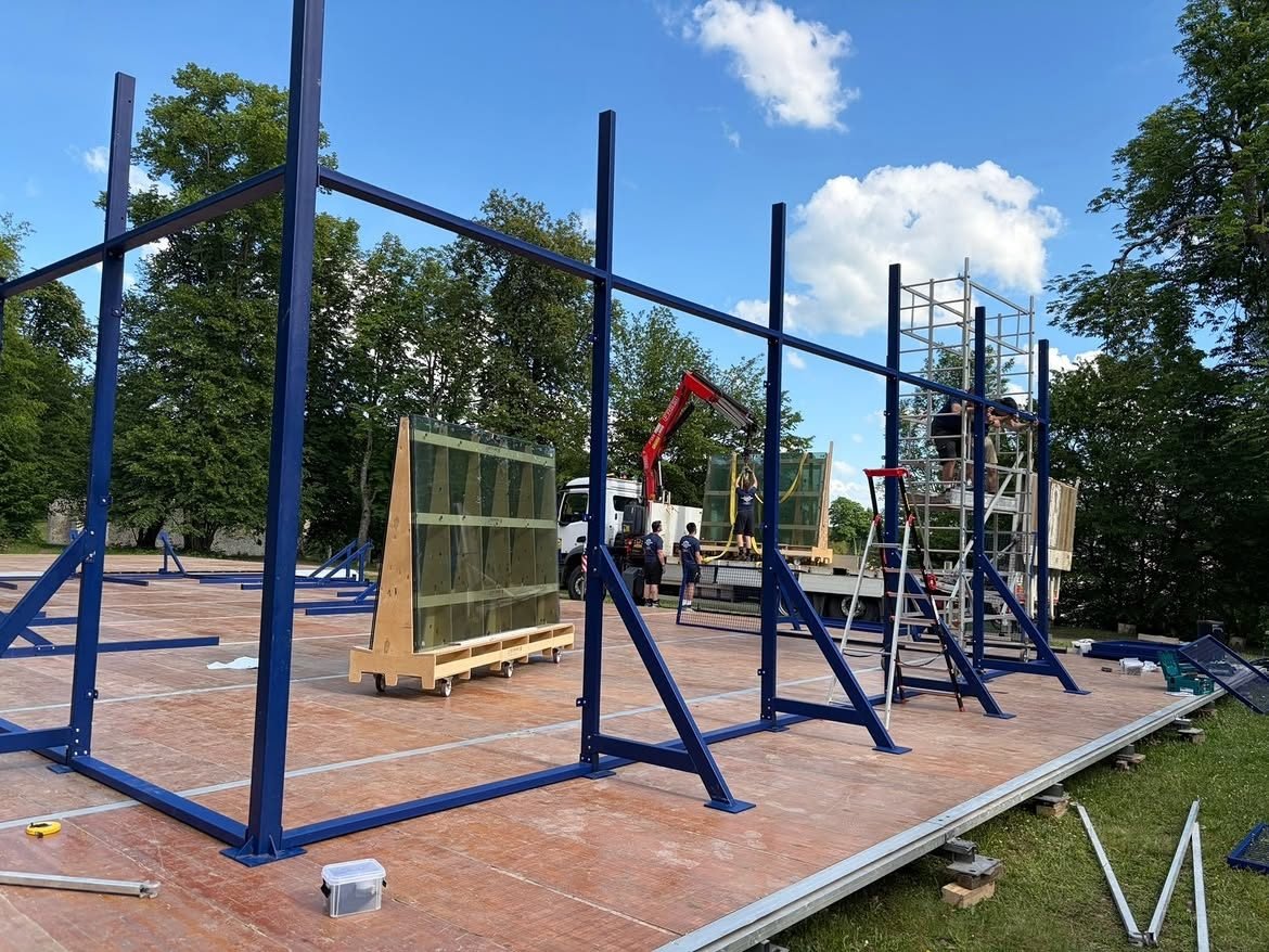 Montage de la structure autoportante : colonnes bleues contreventées, chariot de vitrages et grue de déchargement